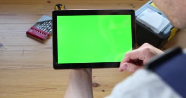 Mavi üniformalı bir tamirci elinde yeşil ekranlı bir tablet tutuyor..