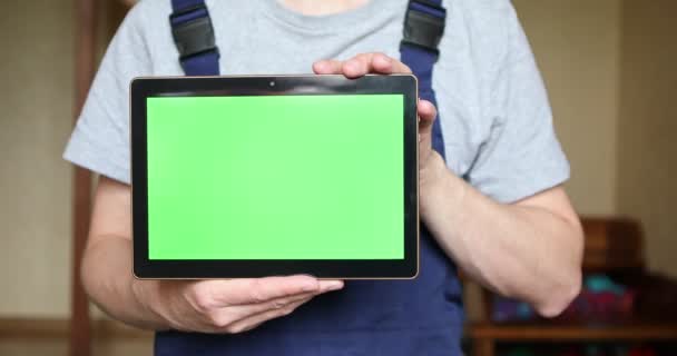 Ein Handwerker in blauer Uniform hält ein Tablet mit grünem Bildschirm in der Hand. — Stockvideo