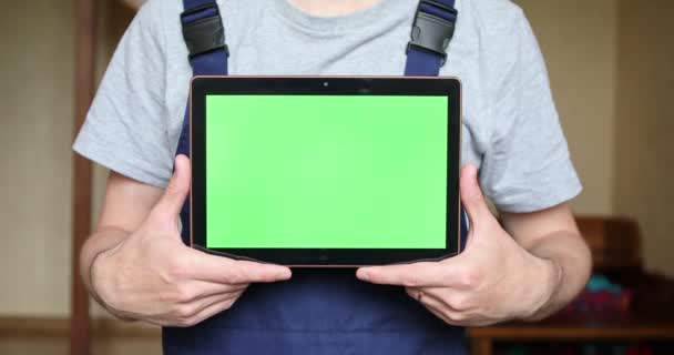 Een klusjesman in een blauw uniform houdt een tablet met een groen scherm in zijn handen. — Stockvideo