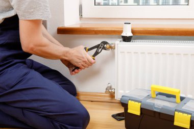 Isıtma radyatörünü tamir et. Adam ingiliz anahtarıyla radyatör onarıyor..