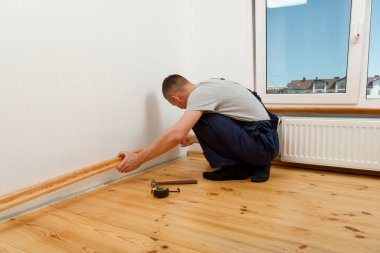 Onarım yapmak için. Yeni bir etek panosu kuruyorum. Bir adam odada tamirat yapar.