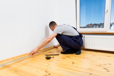 Onarım yapmak için. Yeni bir etek panosu kuruyorum. Bir adam odada tamirat yapar.