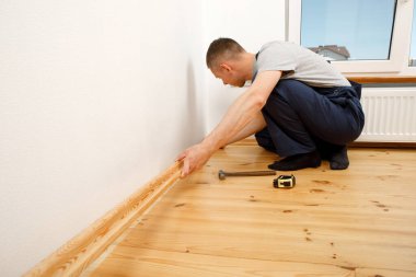 Onarım yapmak için. Yeni bir etek panosu kuruyorum. Bir adam odada tamirat yapar.