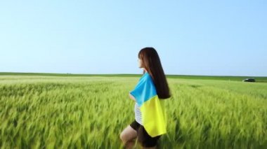 Genç hamile bir kız Ukrayna bayrağıyla neşeyle buğday tarlasında koşuyor.. 