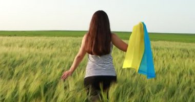Genç hamile bir kız Ukrayna bayrağıyla neşeyle buğday tarlasında koşuyor.. 