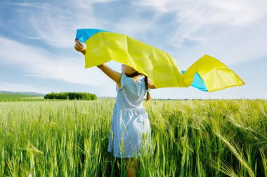Buğday tarlasında Ukrayna bayrağı taşıyan küçük kız. Bağımsızlık Günü 'nü kutlayan mutlu çocuk..