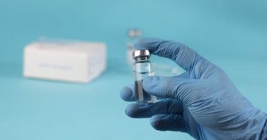 Doktorlar Mavi Eldiven 'de mavi arka planda aşı ya da uyuşturucu bulunan şişeyi tutuyorlar. Aşılama kavramı.