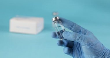 Doktorlar Mavi Eldiven 'de mavi arka planda aşı ya da uyuşturucu bulunan şişeyi tutuyorlar. Aşılama kavramı.
