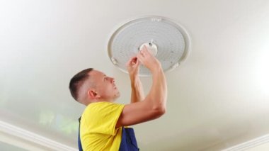 Genç bir adam, bir elektrikçi, avizeyi tamir ediyor, tavandaki lambanın tabanına vida takıyor. Bir dairenin tamiri..
