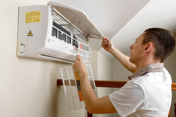 Male technician cleaning air conditioner indoors.