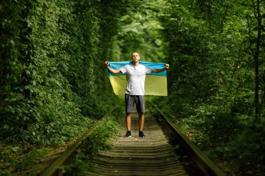 man raised his hands and holds the Ukrainian flag behind his back. concept Ukrainian patriot, rally in support of Ukraine