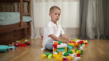 Funny baby boy with educational toy blocks. Children play at day care or preschool. Mess in kids room. Toddlers build a tower in kindergarten. Child playing with colorful toys.