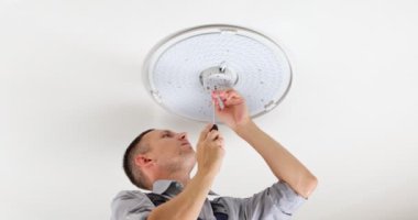 Genç bir adam, bir elektrikçi, avizeyi tamir ediyor, tavandaki lambanın tabanına vida takıyor. Bir dairenin tamiri..