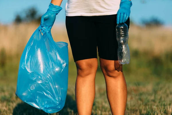 Plastic pollution in the environmental problem of the world. A hand in a blue glove puts garbage in a plastic bag. Removal and cleaning of garbage from contaminated territories