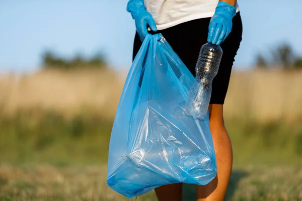 Plastic pollution in the environmental problem of the world. A hand in a blue glove puts garbage in a plastic bag. Removal and cleaning of garbage from contaminated territories