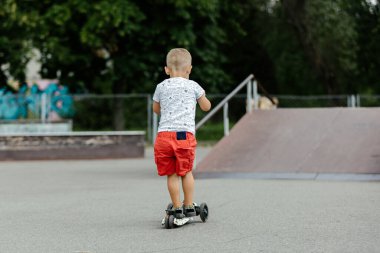 Active boy riding a scooter in the summer skate park