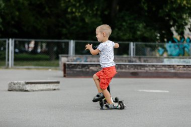 Active boy riding a scooter in the summer skate park
