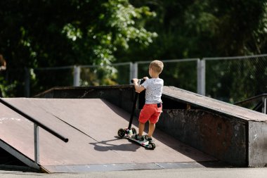Active boy riding a scooter in the summer skate park