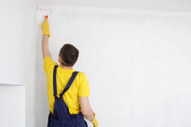 Adam duvarları ve tavanı beyaza boyuyor. Odayı boyuyor ve onarıyor..