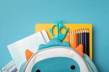 Mavi ve sarı arka planda okul malzemeleriyle dolu bir sırt çantası. Yukarıdan bak. kopyalama alanı. Okul konseptine dönelim..