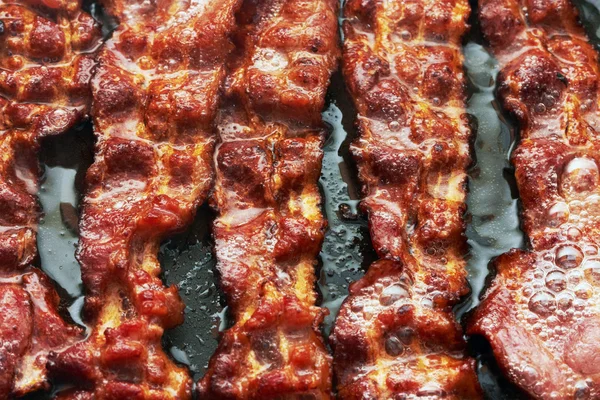 Fatia de bacon sendo cozida na frigideira — Fotografia de Stock