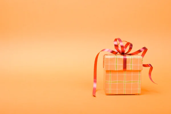 Single orange gift box with red ribbon on yellow background. — Stock Photo, Image