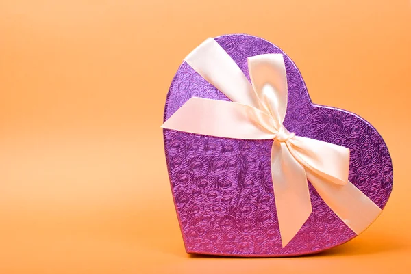 Single heart gift box with ribbon on yellow background. — Stock Photo, Image