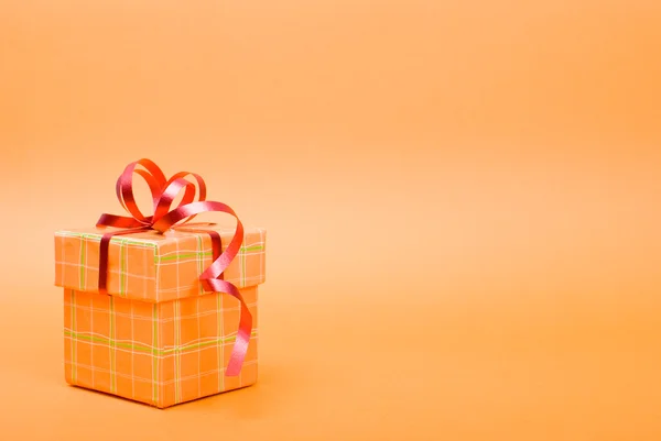 Caja de regalo naranja única con cinta roja sobre fondo amarillo . — Foto de Stock