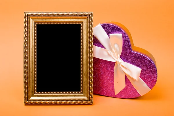 Marco de fotos de oro y caja de regalo de corazón con cinta en fondo naranja —  Fotos de Stock