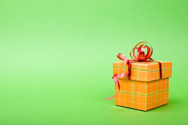 Enkele oranje geschenkdoos met rood lint op groene achtergrond. — Stockfoto