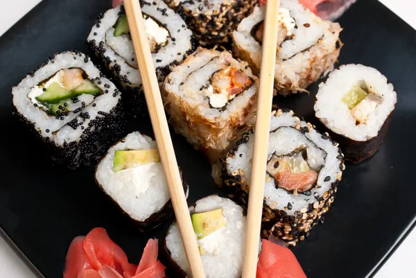Sushi em uma chapa preta na mesa branca . — Fotografia de Stock