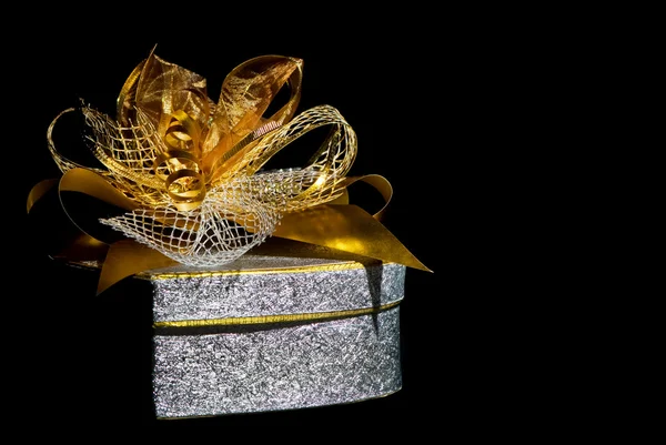 Einzelne silberne Geschenkbox mit goldenem Band auf schwarzem Hintergrund. Stockbild