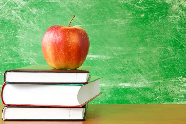 Books with apple against dirty chalkboard — Stock Photo, Image