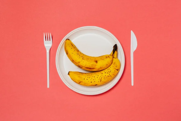 熟したバナナの白いプレートとピンクの背景にナイフでフォーク 健康的な食事 — ストック写真