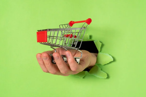 Hand Met Winkelwagentjes Uit Een Gescheurd Gat Groen Papier — Stockfoto