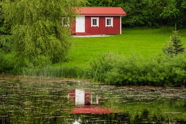池の水に反射して赤い休日のキャビンで表示します 木製のコテージ 海岸のサウナ 水の近くの小さな家 緑の木々に囲まれた建物 — ストック写真
