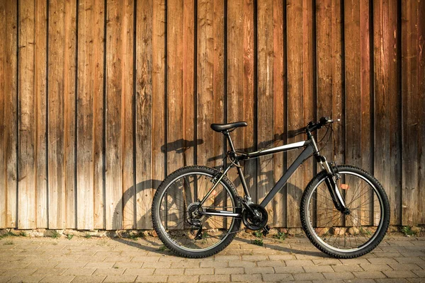 Modern sport mountain bike leaning against brown wooden wall. Active lifestyle.