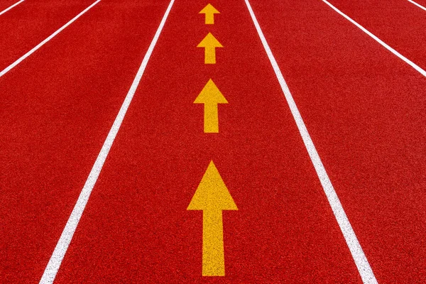 Outdoors stadium running red tartan track with white straight arrow symbols. Keep Moving Forward.