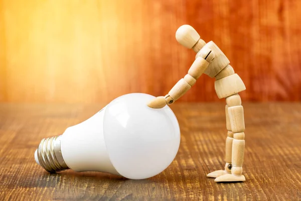 Wooden dummy with LED light bulb on wooden background. Conceptual image.