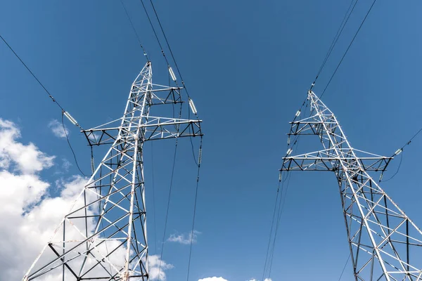 Electricity transmission power lines (High voltage towers). High voltage pylons with electricity transmission power lines against blue sky