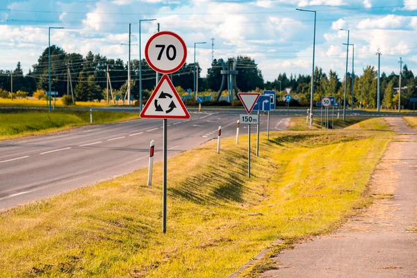 Highway with speed limit 70 road sign, roundabout ahead. Many road signs on the way.