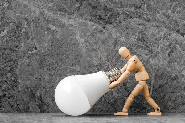 Wooden dummy with economical LED light bulb on stone background. Conceptual image.