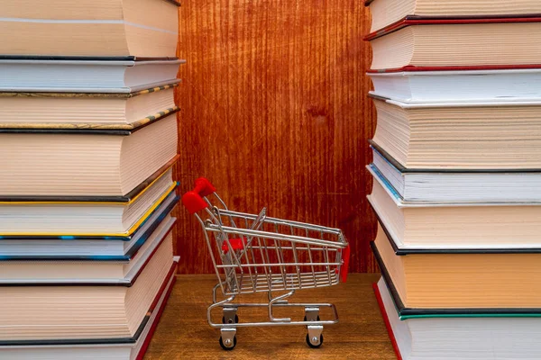 An empty shopping cart between stacked books. The concept of buying books in a bookstore or online.
