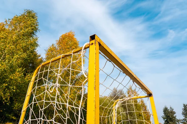 Corner of small football goal. Triangle with net of yellow goal in soccer field - close up.