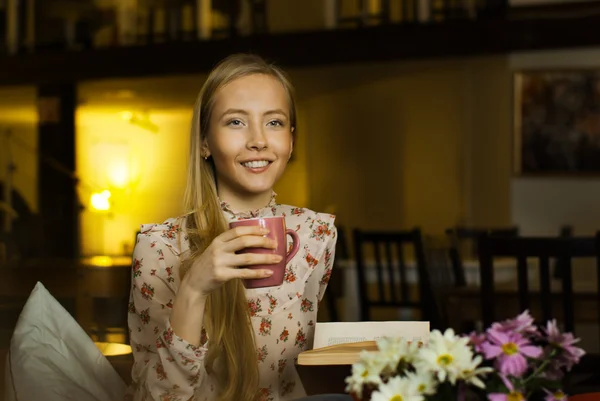 Vacker flicka med en kopp i ett café som läser en bok — Stockfoto