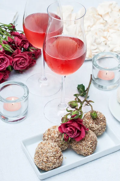 Two glasses of rose wine , fresh flowers, cakes
