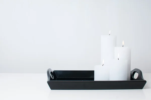 Four white candles burning on a black tray