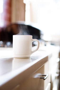 Mutfak masasında beyaz silindir bardak ve gerçek gün ışığı.