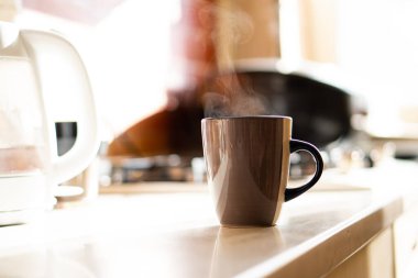 Kahverengi kahve fincanı mutfak masasının üzerinde gerçek gün ışığı ve buharla