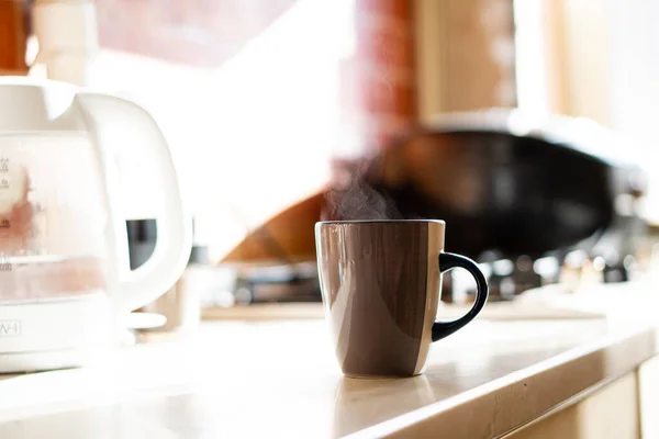 Taza de café marrón en la mesa de la cocina con luz natural real y vapor — Foto de Stock